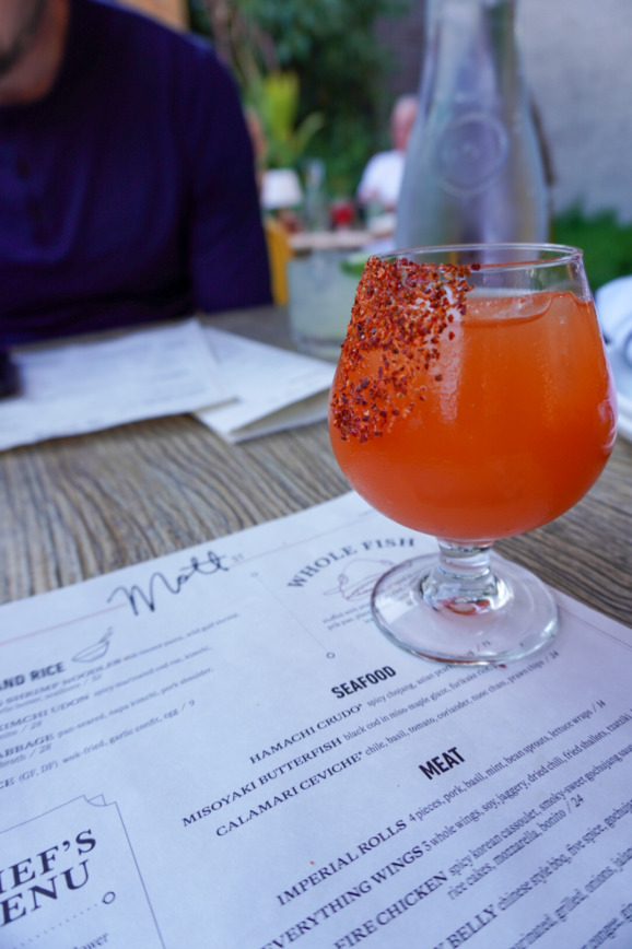 Vibrant orange cocktail with chili rim on a patio table at Mott St in Chicago, Illinois.