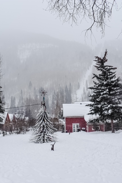 Snow-covered red cottage and pine trees in Telluride, framed by misty mountains and soft winter light.