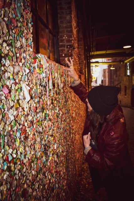 Visitor adding gum to the colorful Gum Wall in Seattle’s Post Alley.