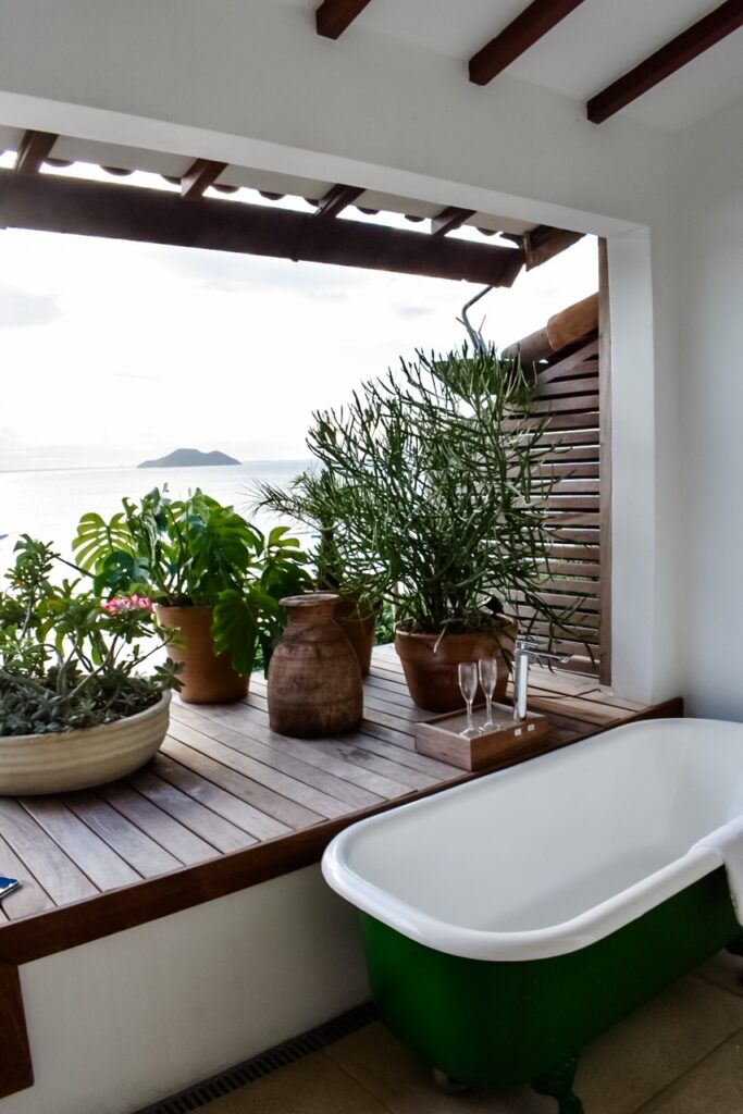 Outdoor balcony tub surrounded by potted plants overlooking the ocean.