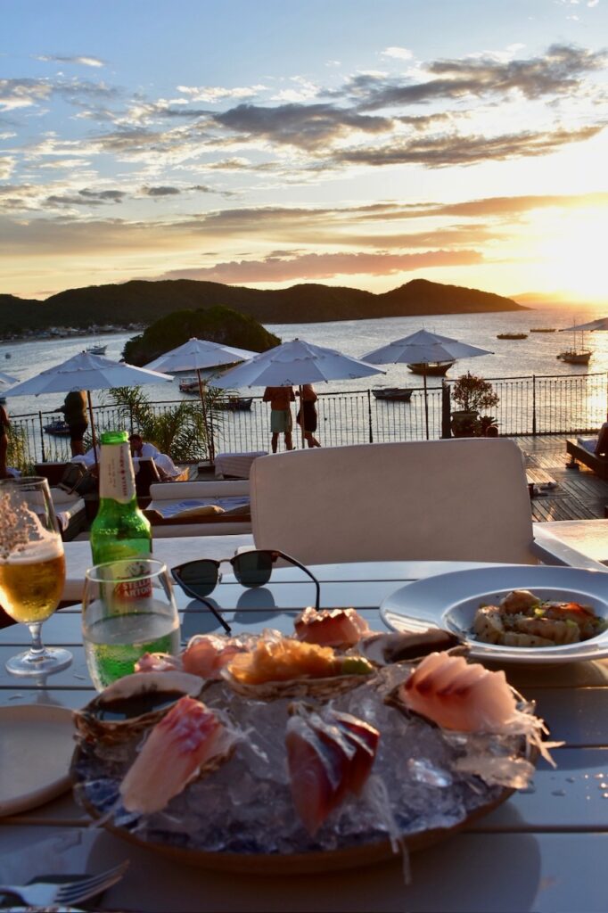 Seafood and drinks by the ocean at sunset with umbrellas and mountain views.