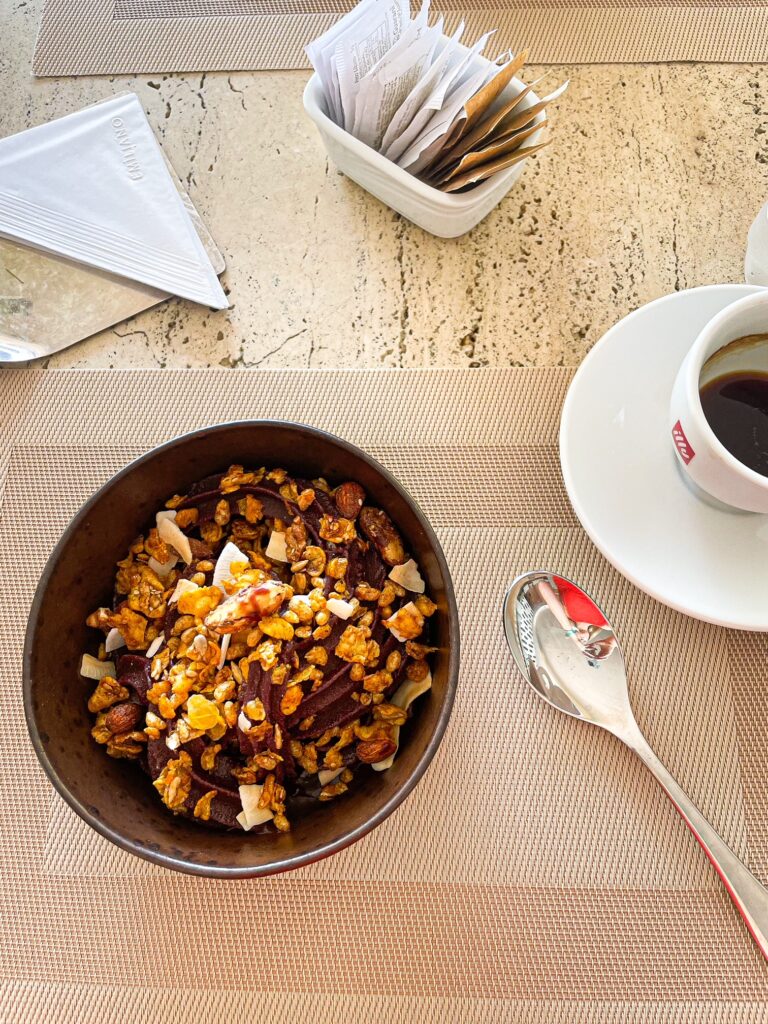 Bowl of granola with coffee on a marble table set for breakfast.