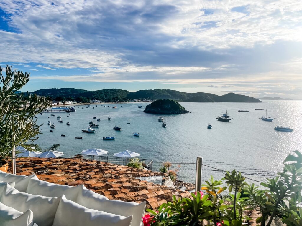 Scenic coastal view of Búzios, Brazil, with boats anchored in the bay and lush green hills under a partly cloudy sky