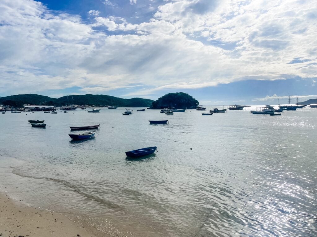 Small fishing boats floating in the calm, sunlit waters of Armação Bay in Búzios, Brazil.