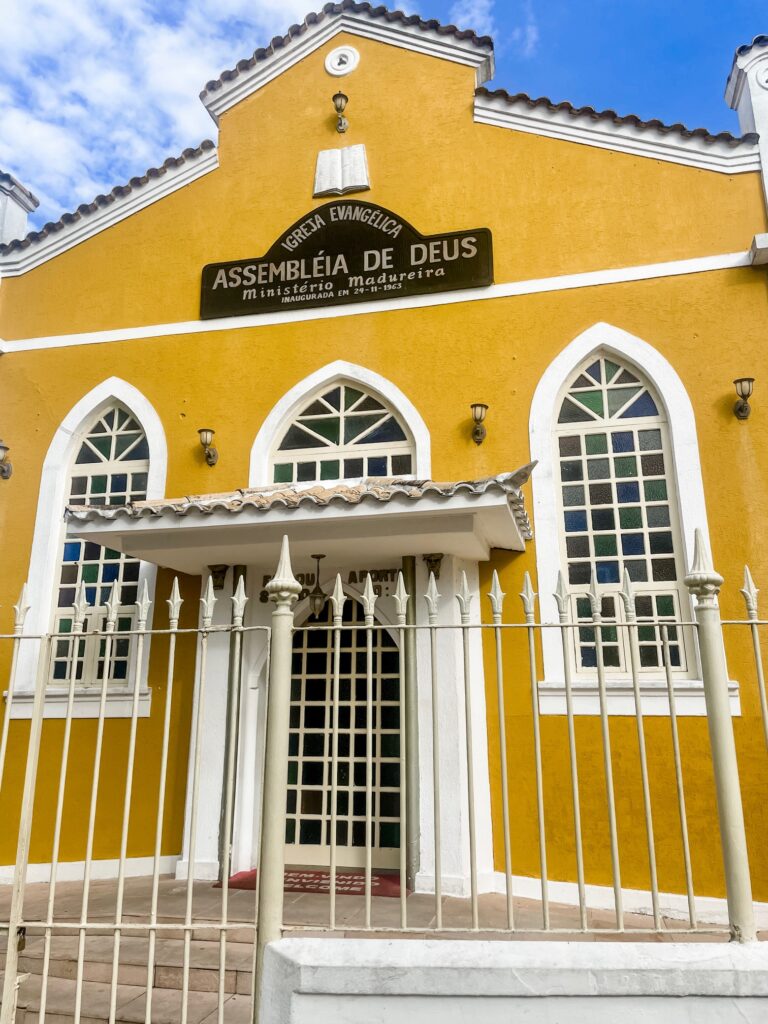 Yellow church facade with arched windows and white trim under a bright blue sky.