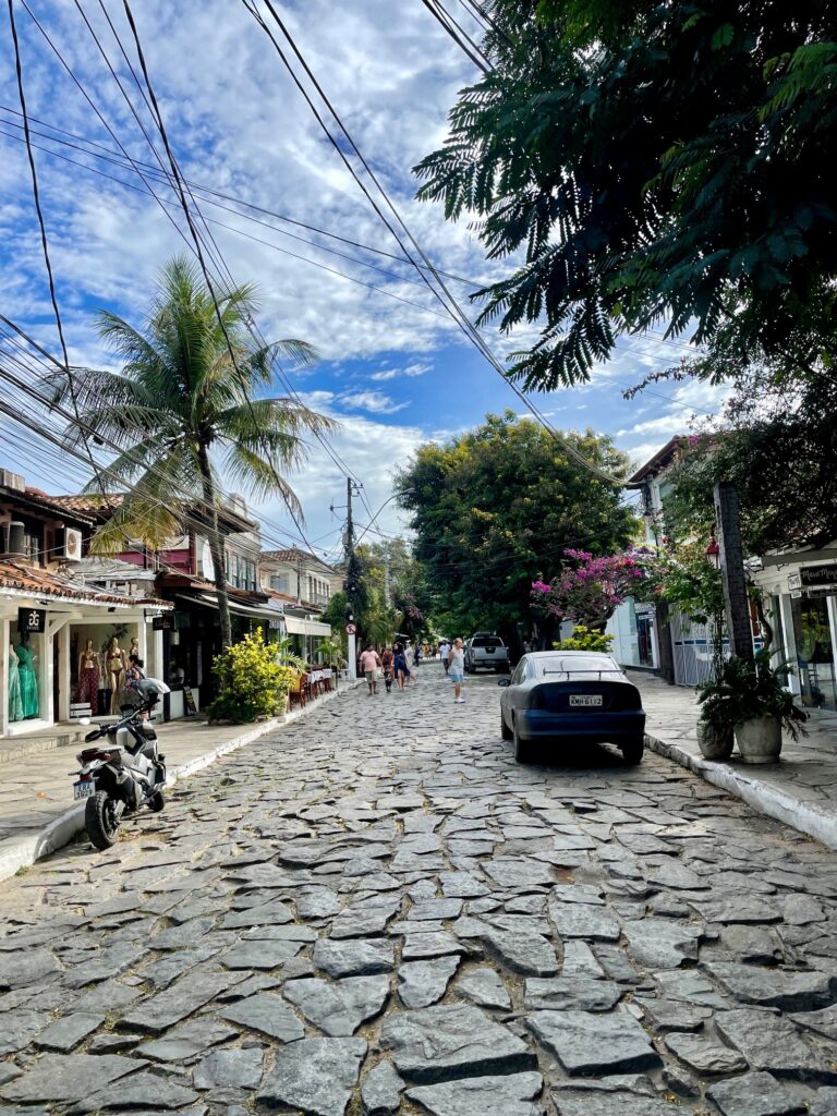 Cobbled street lined with shops, palm trees, and pedestrians in the tropical town of Búzios