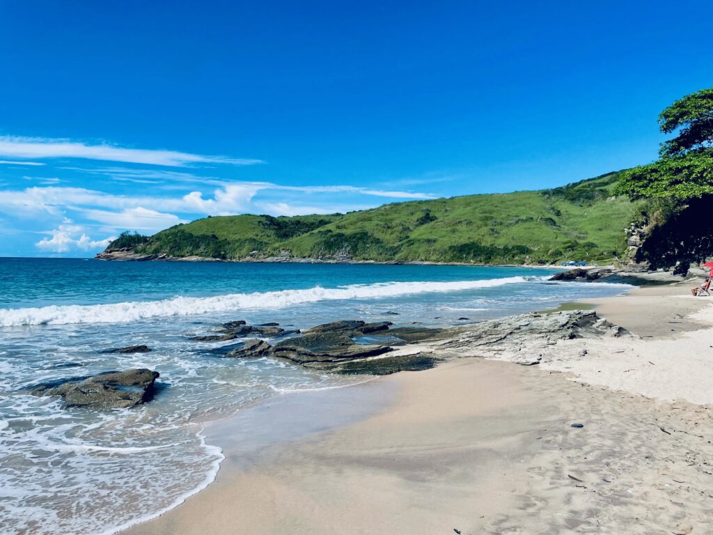 Peaceful Brava Beach with turquoise waves, rocky shore, and green hills under a bright blue sky.