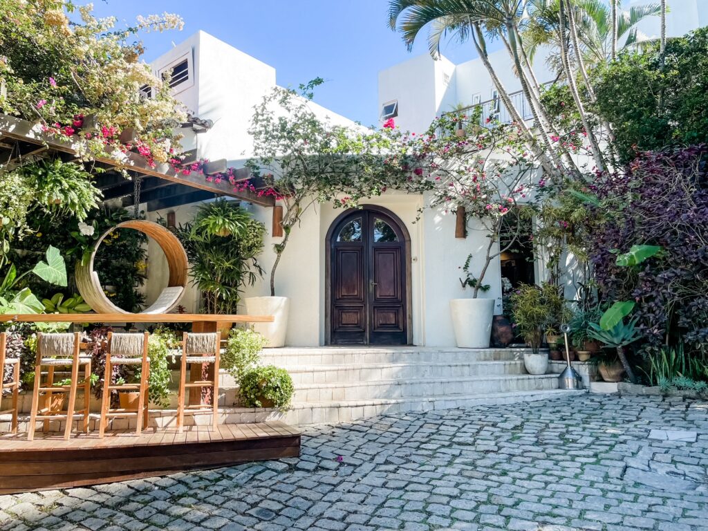 Charming courtyard entrance to Casas Brancas with wooden doors, lush plants, and outdoor bar seating under flowering vines.