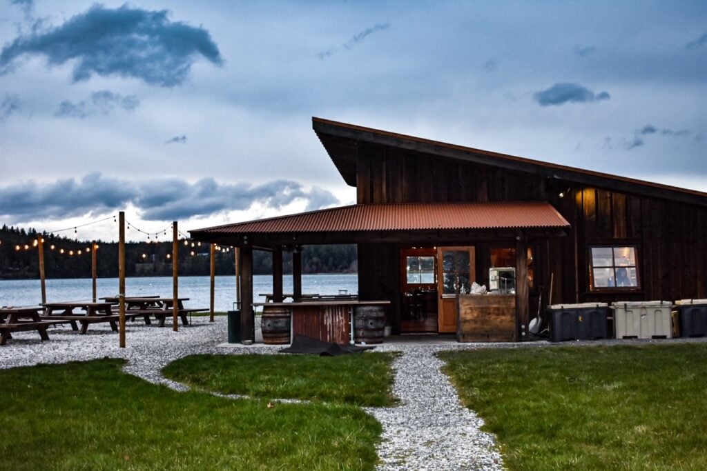 Cozy lakeside cabin with string lights and picnic tables at dusk under a moody sky.