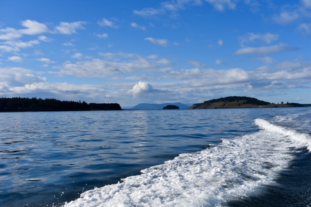 Boat wake cutting through calm blue water with forested islands and clouds on the horizon.