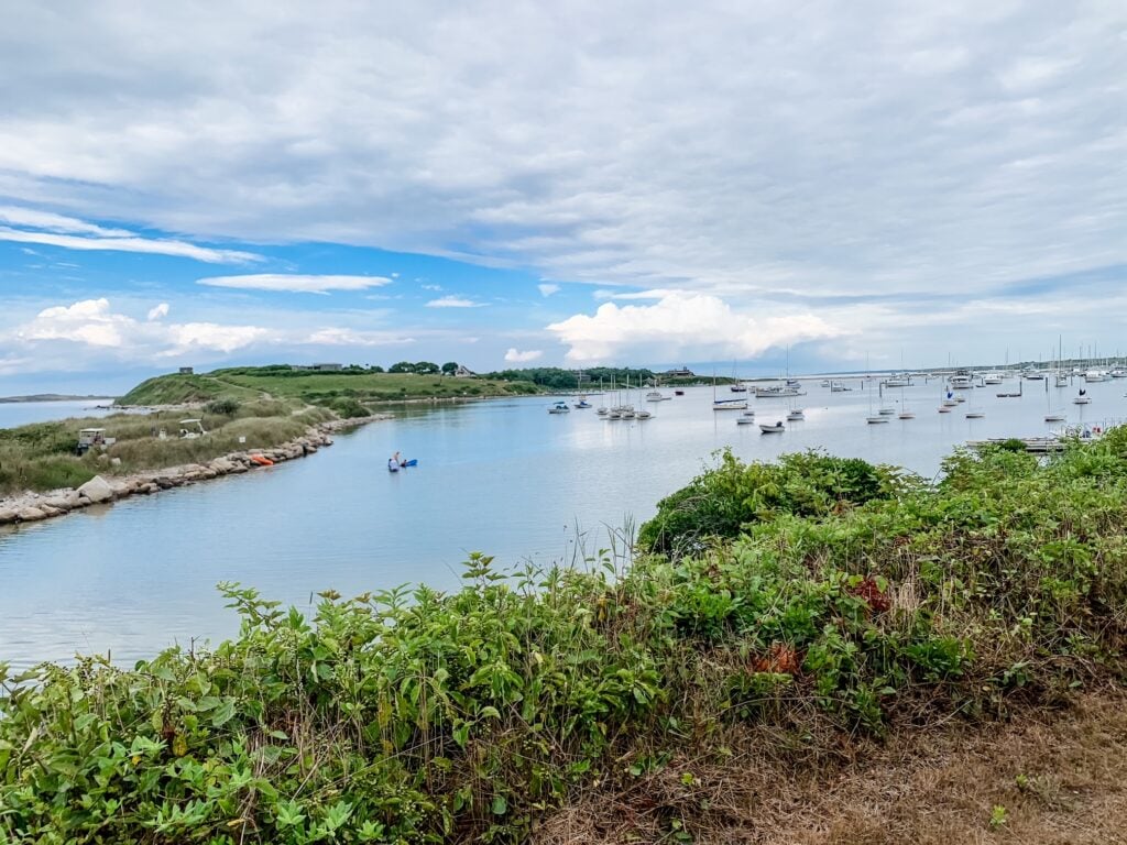 Boats anchored in the calm harbor at Cuttyhunk Island under a partly cloudy sky.