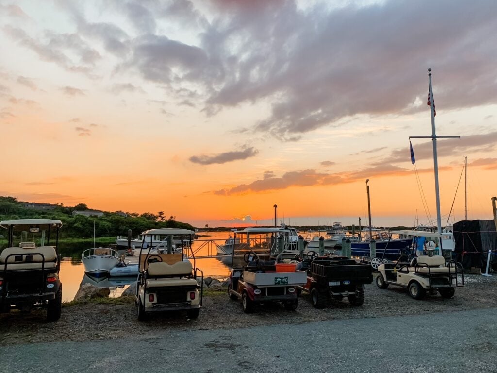 Golf carts and boats parked by the Cuttyhunk harbor at sunset under a colorful orange and purple sky