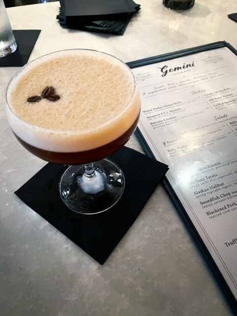 An espresso martini in a chilled martini glass, with foam on the top and garnished with three espresso beans at Gemini's indoor bar