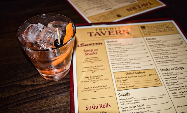 Old Fashioned cocktail with orange peel and cherry beside a menu at Trivoli Tavern, a cozy Chicago restaurant.