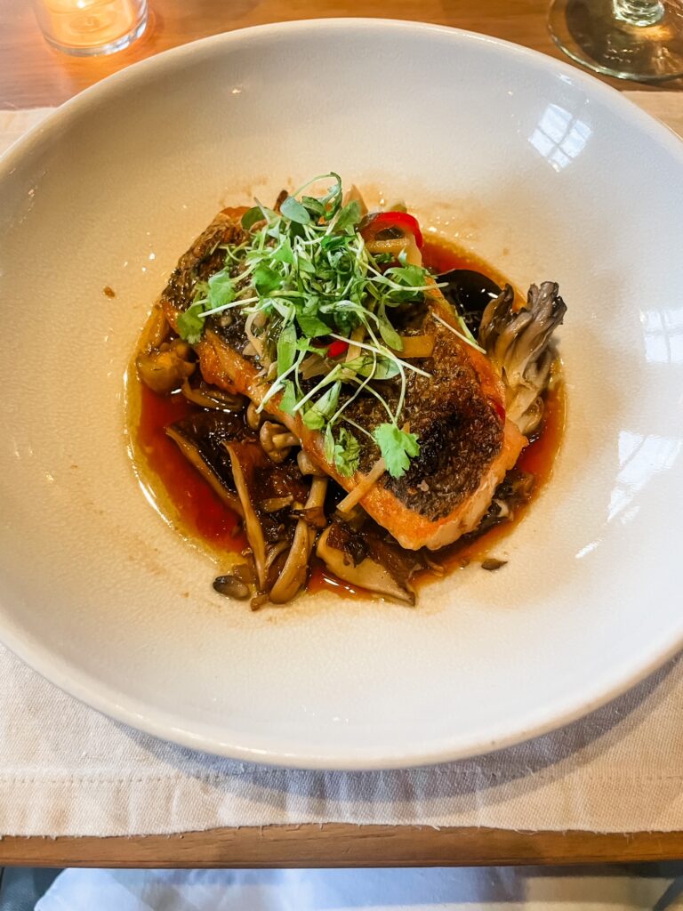Seared fish with mushrooms and microgreens in a tangy sauce.