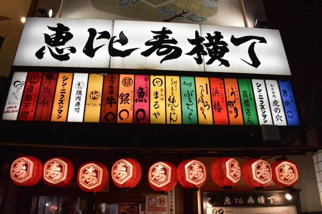 Colorful lantern-lit entrance to an izakaya alley in Ebisu, Tokyo, with Japanese signs glowing at night