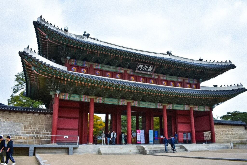 Ornate wooden gate at Changdeokgung Palace featuring red columns and green-tiled eaves.