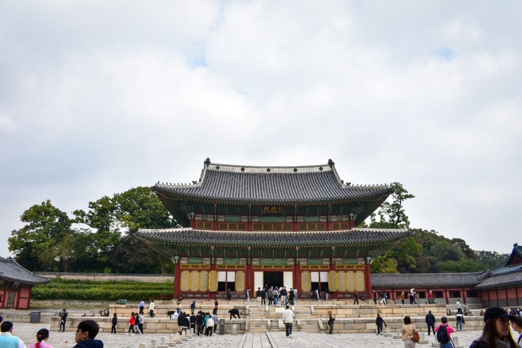 Main hall of Changdeokgung Palace with ornate eaves and visitors gathered below.