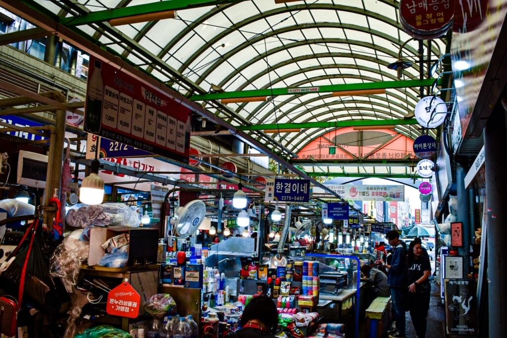 Bustling covered walkway at Gwangjang Market lined with food stalls and colorful signs.
