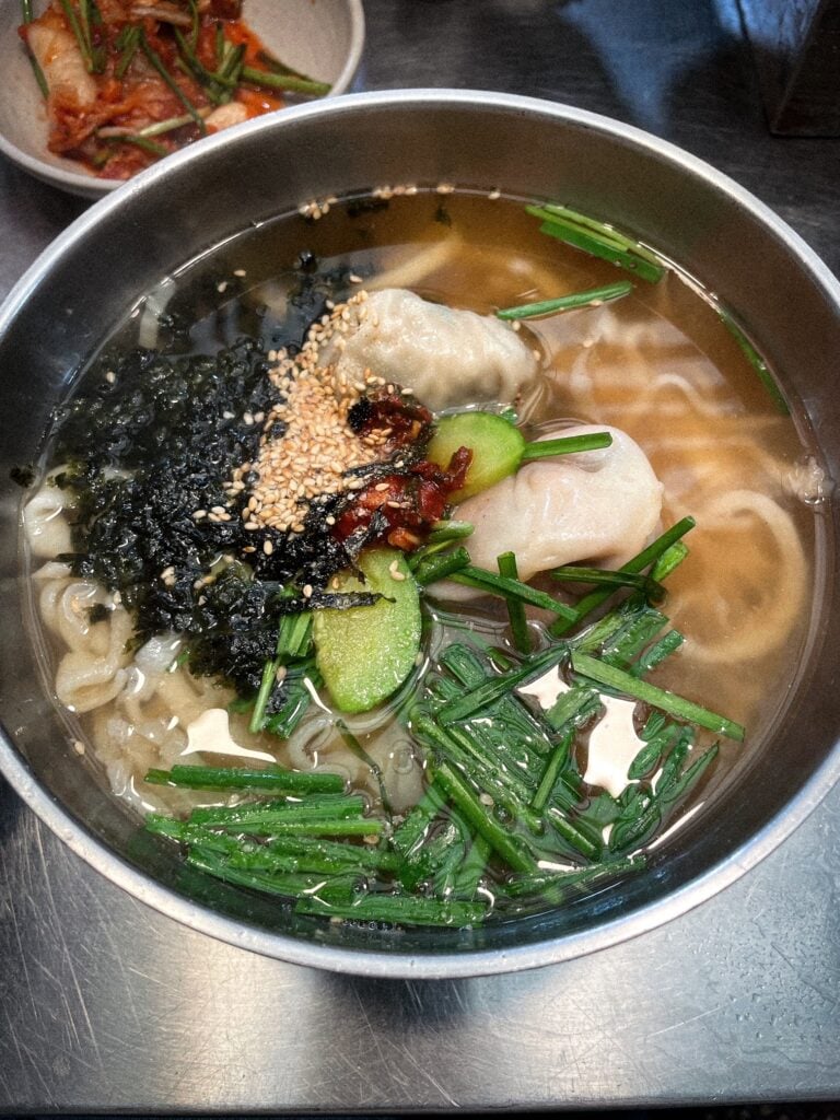 Korean udon noodle soup with dumplings, seaweed, and sesame seeds.