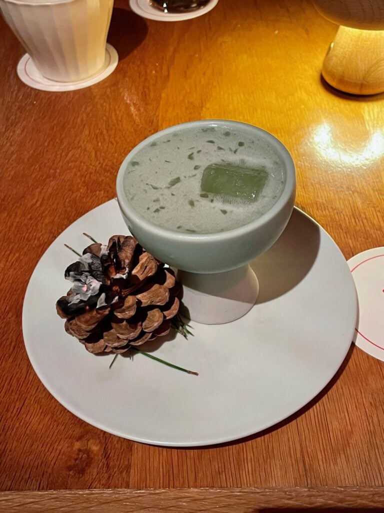 Refreshing green cocktail served in a ceramic cup with a pinecone garnish on the side.