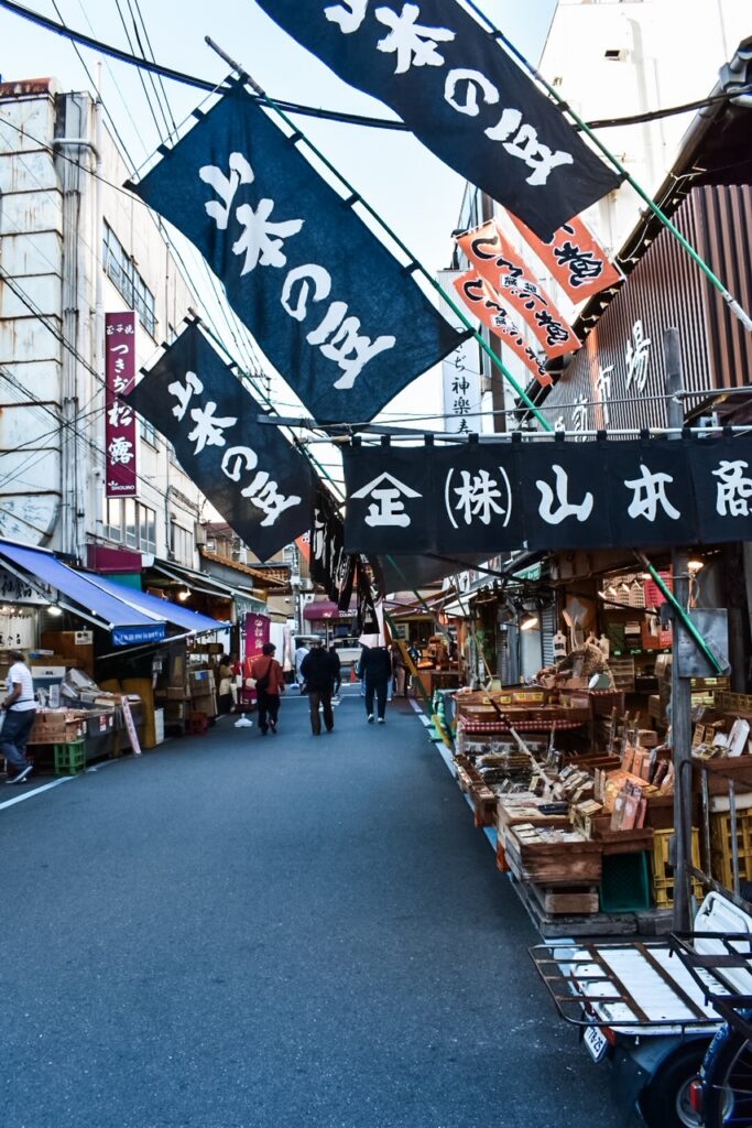 Morning scene at Tsukiji Outer Market in Tokyo, where lanterns glow above seafood stalls and narrow market streets