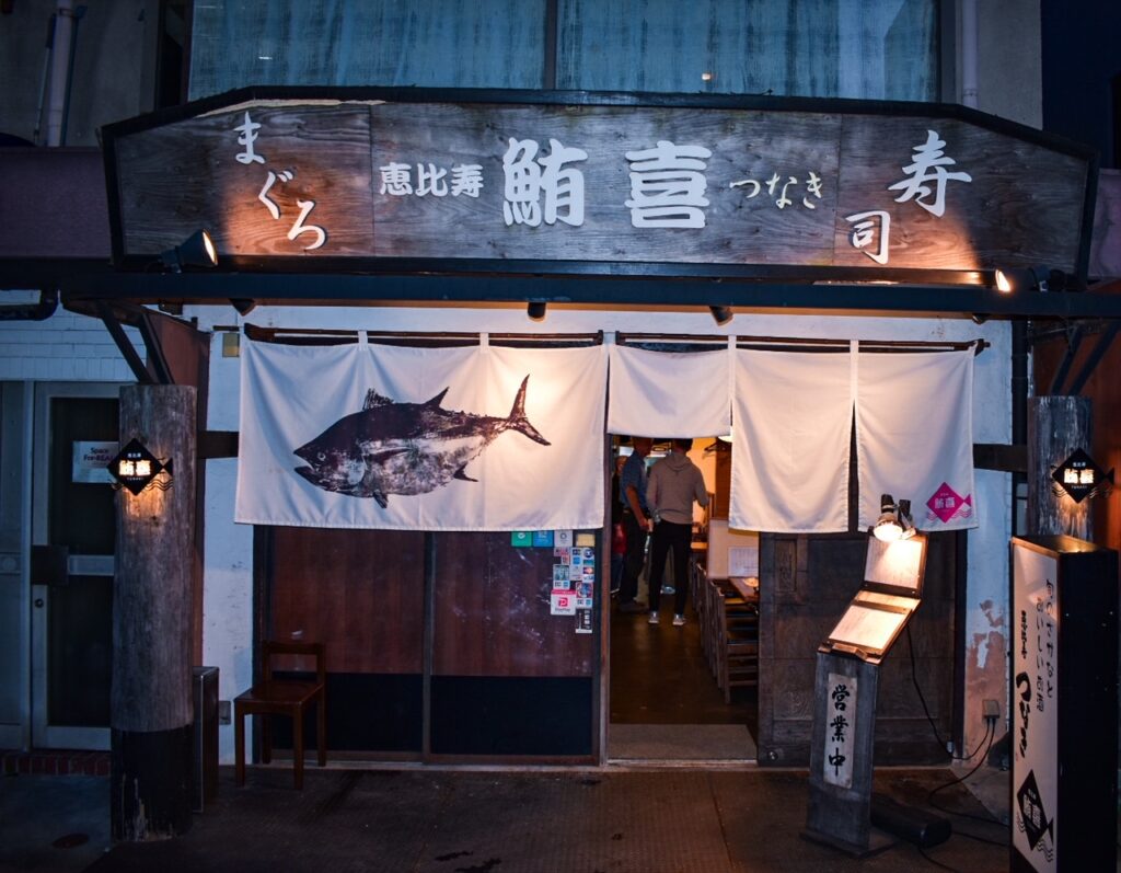 Wooden-front izakaya in Ebisu, Tokyo, with a curtain featuring a large tuna illustration at the entrance.