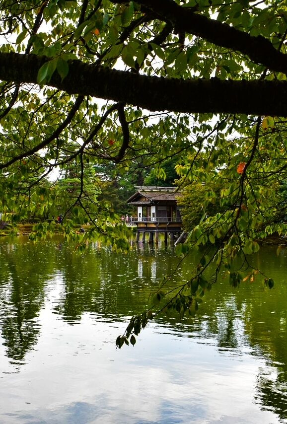 Traditional teahouse overlooking a peaceful pond surrounded by greenery in Kenrokuen Garden, Kanazawa, Japan