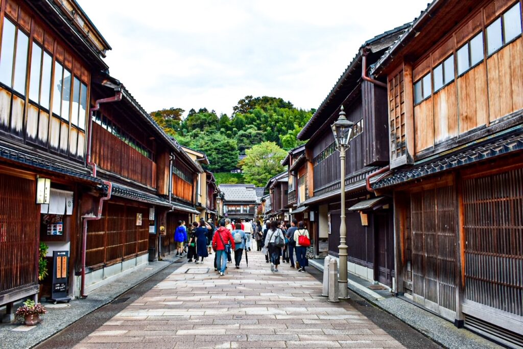 Visitors walking through a narrow stone-paved street lined with traditional wooden teahouses in Kanazawa’s historic geisha district.