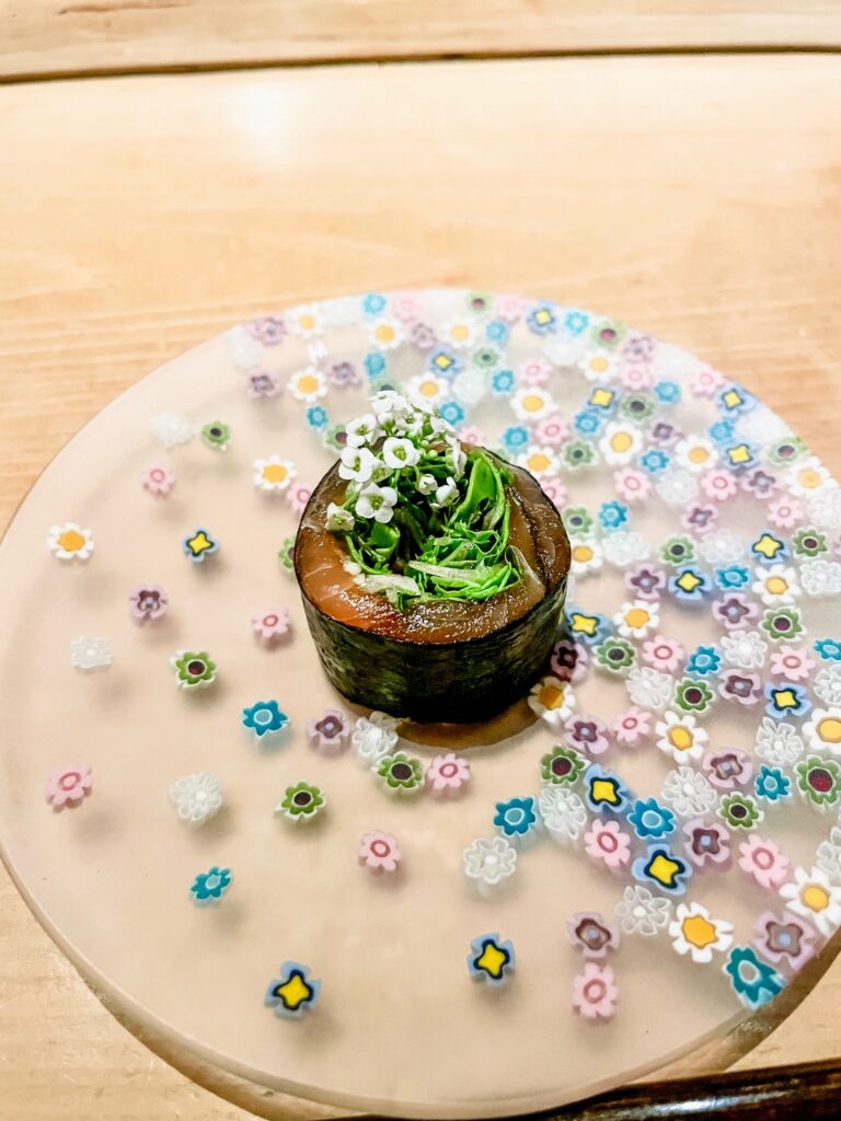 Sushi roll garnished with greens and white flowers on a pastel floral-patterned plate.