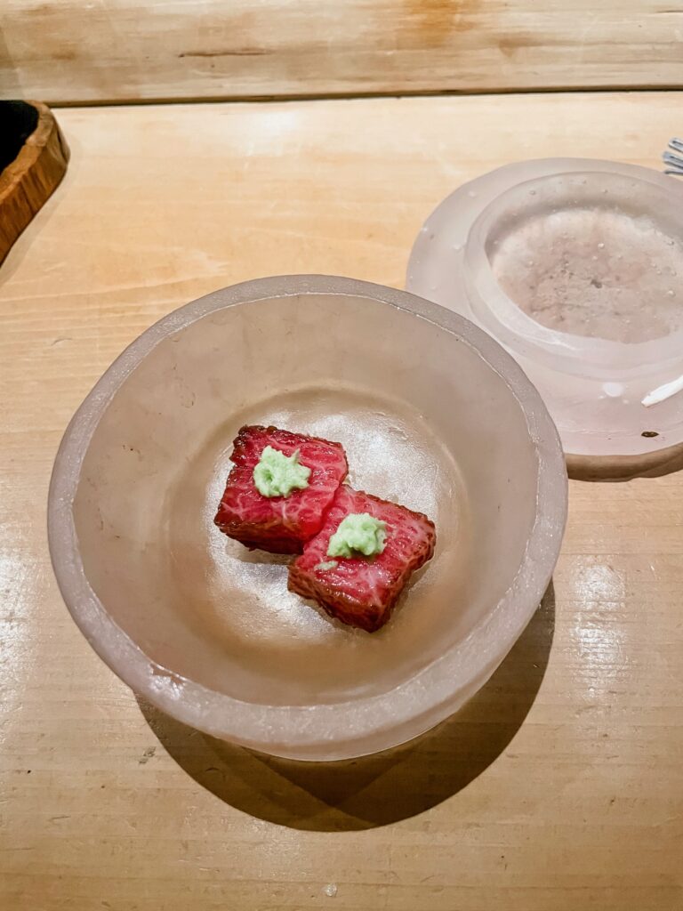 Two pieces of seared Wagyu topped with wasabi in a frosted bowl.