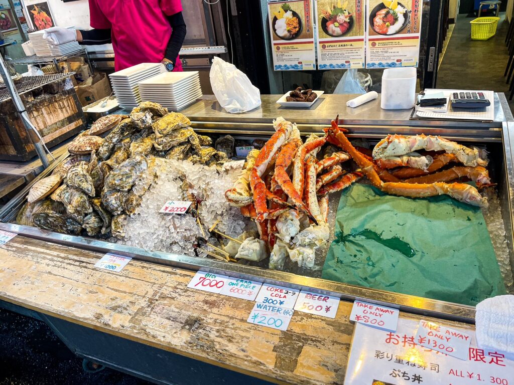 Seafood stall displaying crab legs and oysters on ice with handwritten price tags.