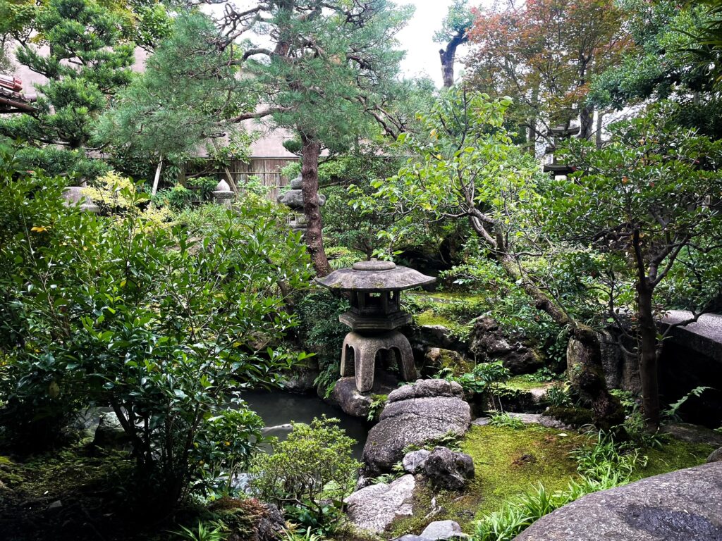 Traditional Japanese garden with a stone lantern surrounded by moss, rocks, and greenery in the samurai district.