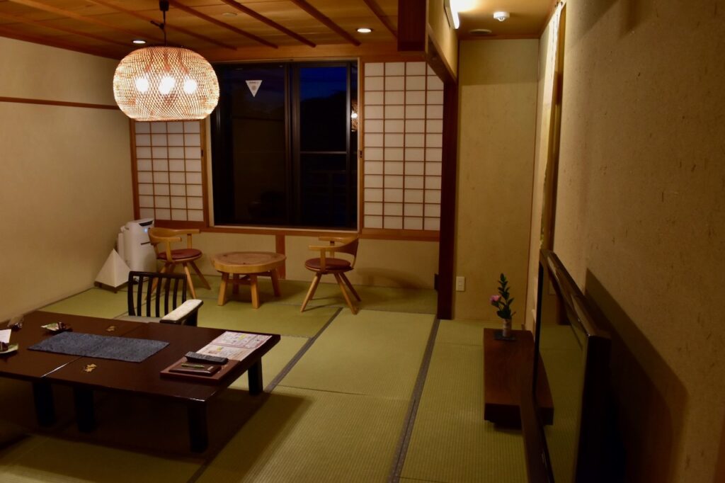 A traditional Japanese ryokan room with low wooden furniture, shoji sliding screens, and soft warm lighting creating a calm, minimalist atmosphere.