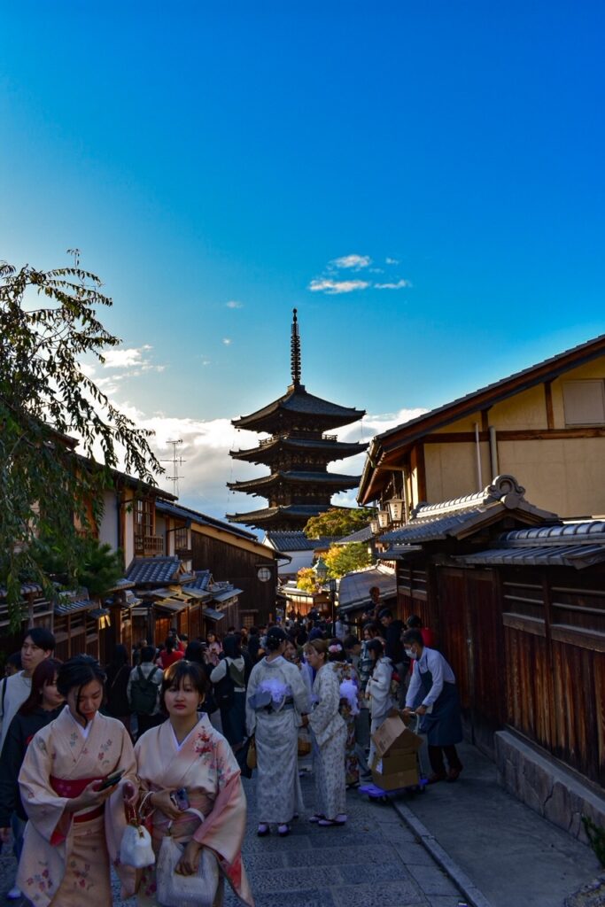 Crowds walking through Kyoto’s old town streets with Yasaka Pagoda rising in the background at sunset