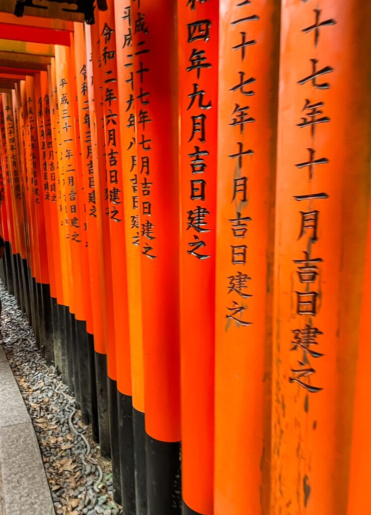 The iconic vermilion torii gates of Fushimi Inari Shrine, covered in black kanji inscriptions, forming a striking tunnel pathway.
