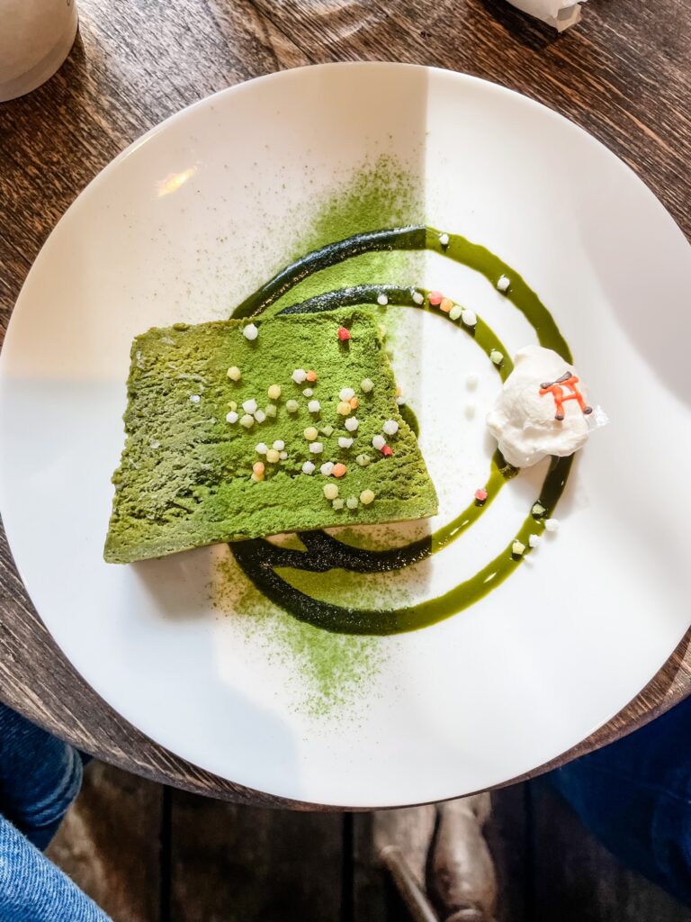 A beautifully plated slice of matcha cake garnished with colorful sugar pearls and cream at Vermillion Cafe.