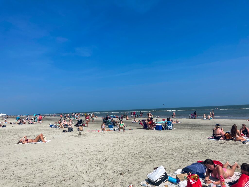 Crowds relaxing and sunbathing on Sullivan's Islands beach under a clear blue sky by the ocean.