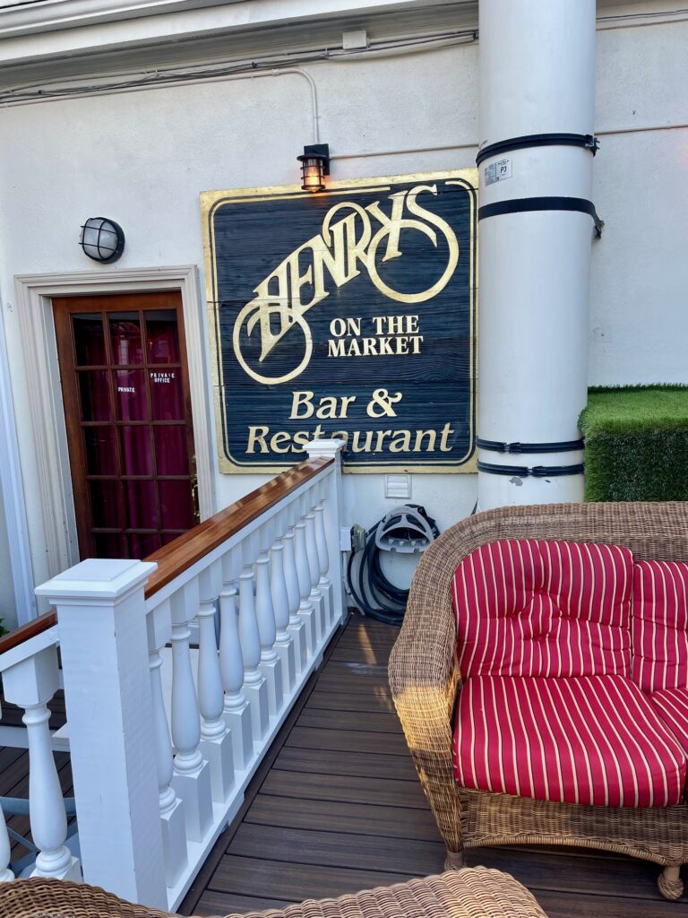 Outdoor patio at Henry’s on the Market with wicker seating and a gold-lettered restaurant sign.