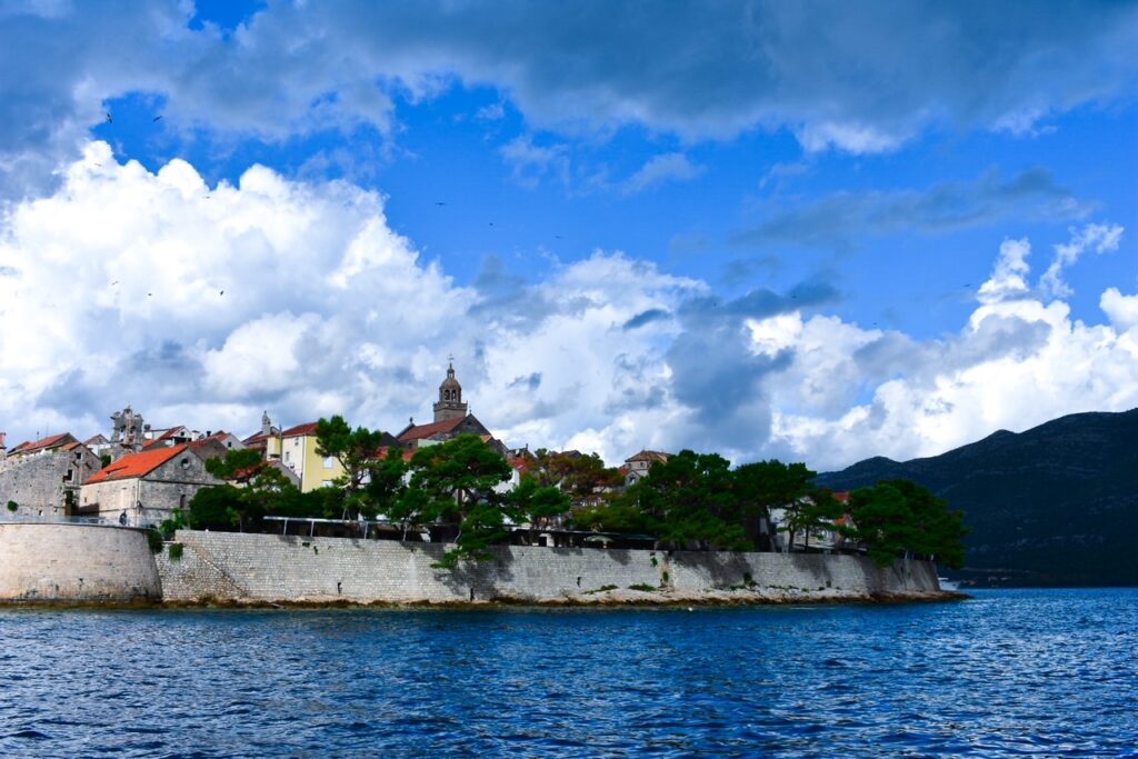 Historic seaside town on Korčula Island with stone walls, red-roofed buildings, and a church tower under dramatic skies.