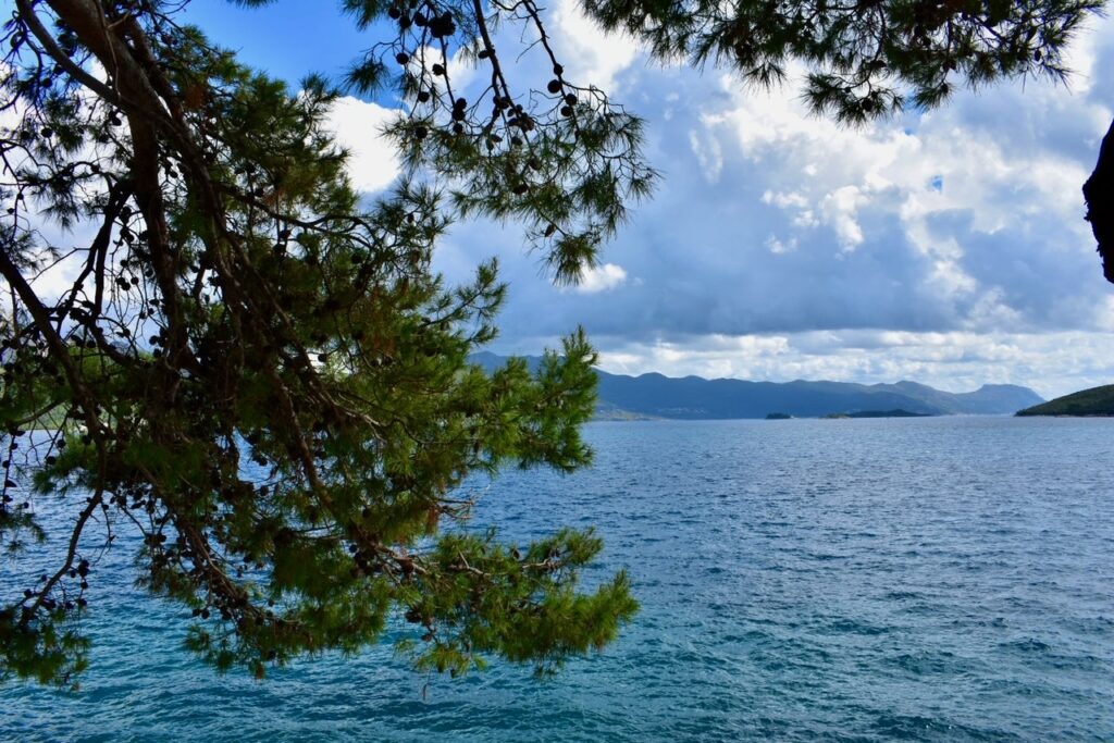 View of the Adriatic Sea framed by pine branches, with distant islands and mountains under a partly cloudy sky.