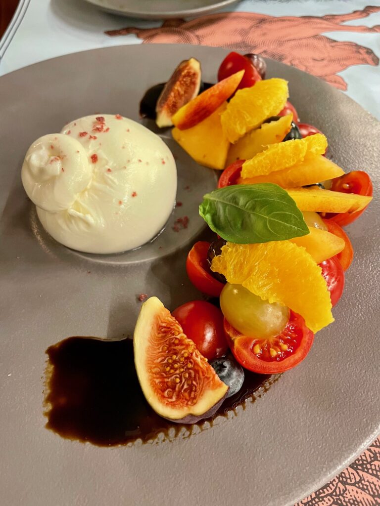 A plate with burrata with figs, oranges, and tomatoes drizzled with balsamic