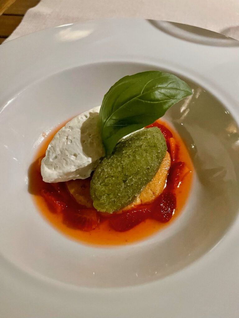 Elegant dessert topped with basil, featuring layers of mousse, fruit, and sauce for a refined finish.
