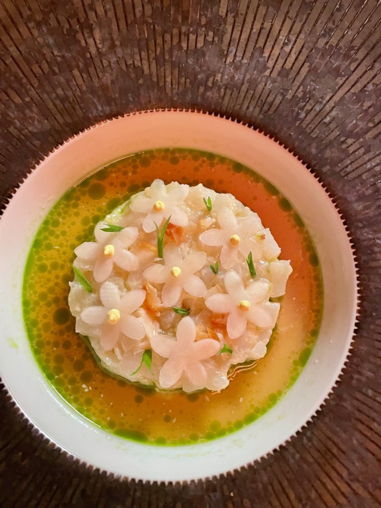 Elegant seafood dish topped with delicate flower-shaped garnishes in green sauce.