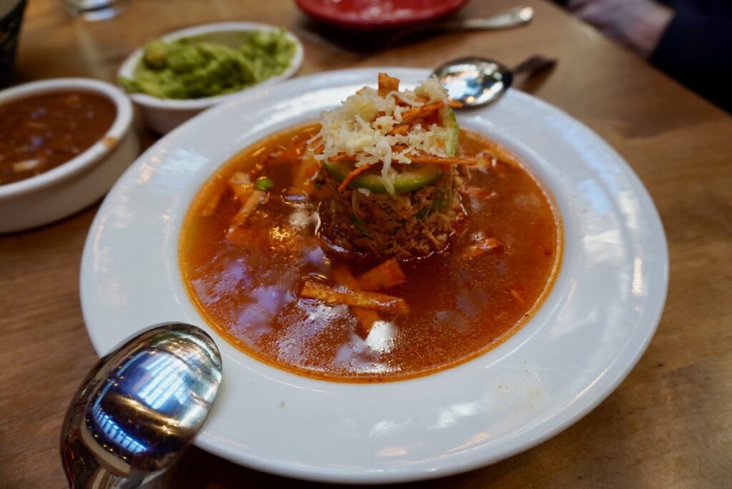 Authentic Mexican tortilla soup topped with avocado and shredded cheese
