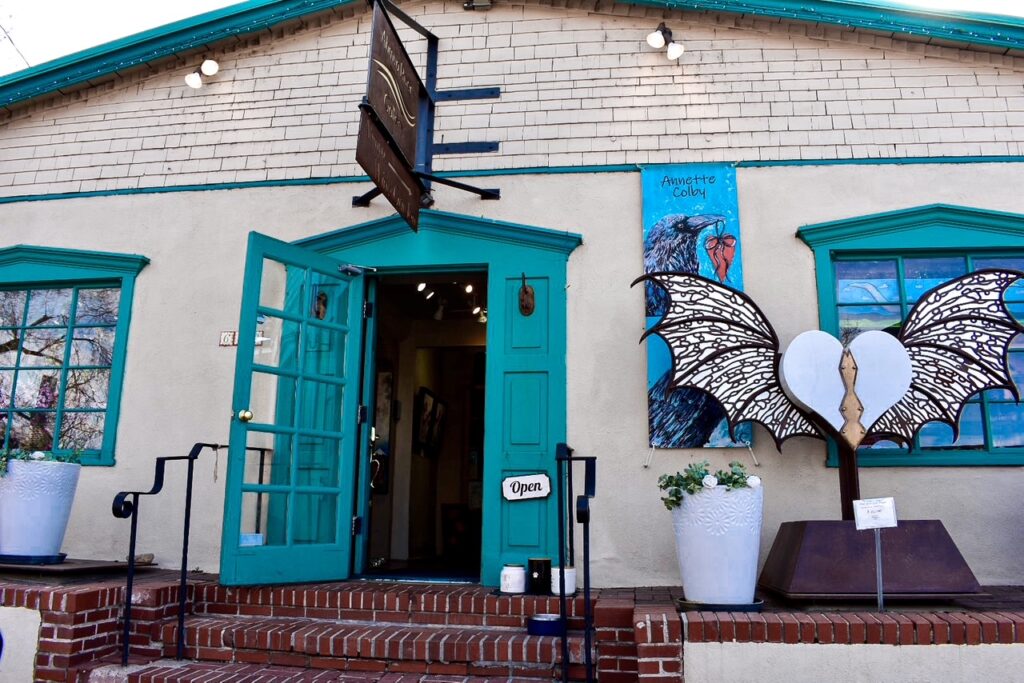 Exterior of Annette Colby Art Gallery in Santa Fe, New Mexico, with turquoise doors and wing sculpture display