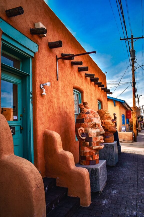 Colorful adobe art gallery with brick head sculptures along Canyon Road in Santa Fe, New Mexico.