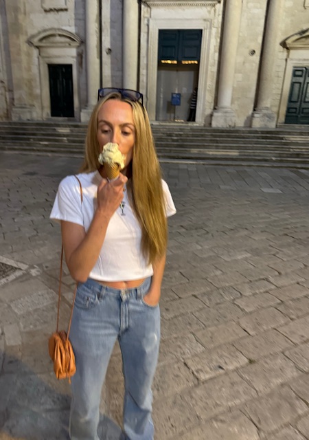 Me enjoying gelato on a cobblestone street in Croatia, standing in front of a historic stone building