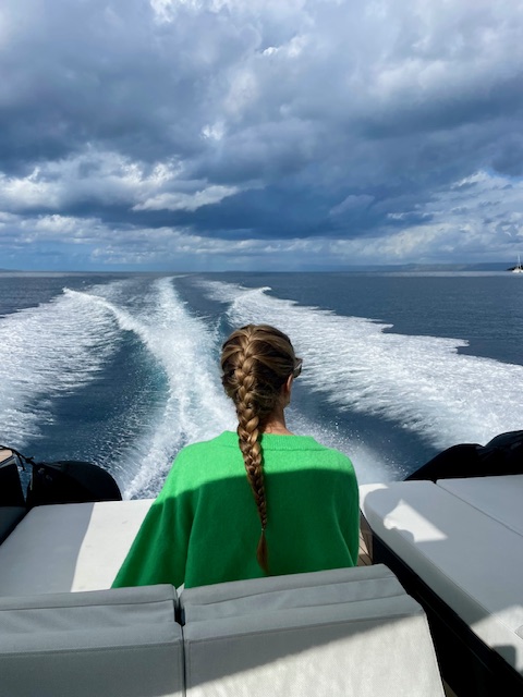 Me sitting on a boat with a French braid, watching the wake trail across the blue sea beneath a cloudy sky