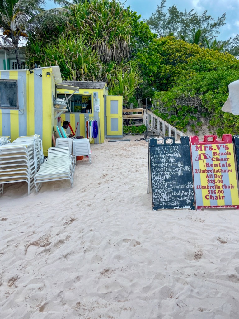Mrs. V’s Beach Bar on Pink Sand Beach, Harbour Island, Bahamas, with colorful signs and lounge chairs.